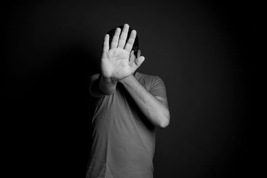 A black and white image of an adult male with a hand raised against a dark background.