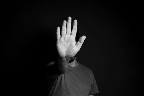 Free A person in the shadows raises a hand as a stop gesture in black and white. Stock Photo