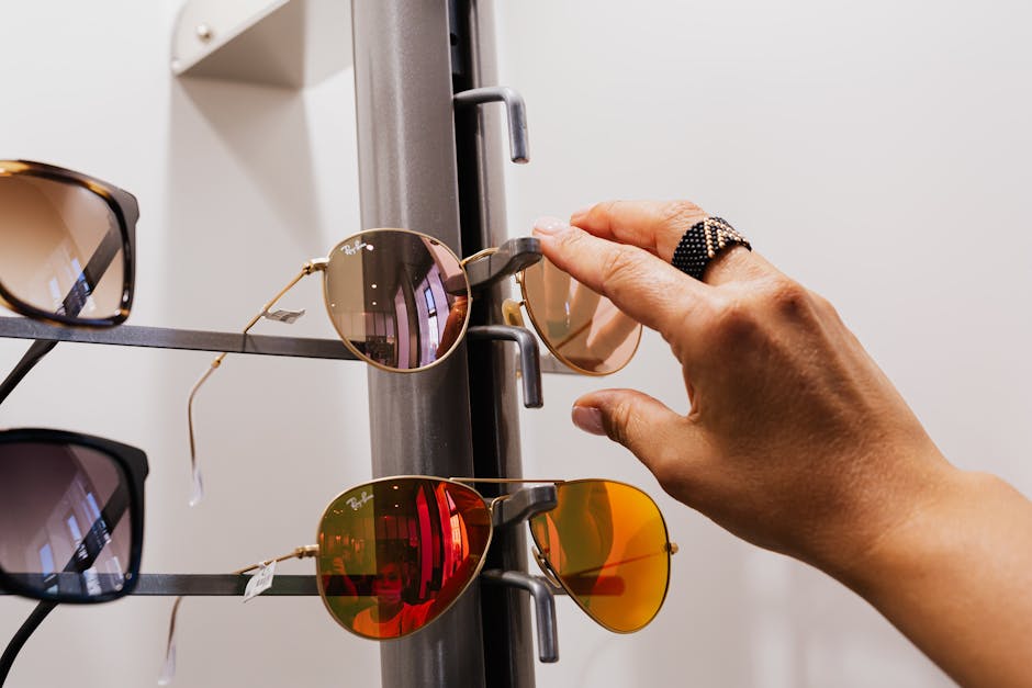 Close-up of a hand selecting sunglasses from a retail display with multiple choices available.
