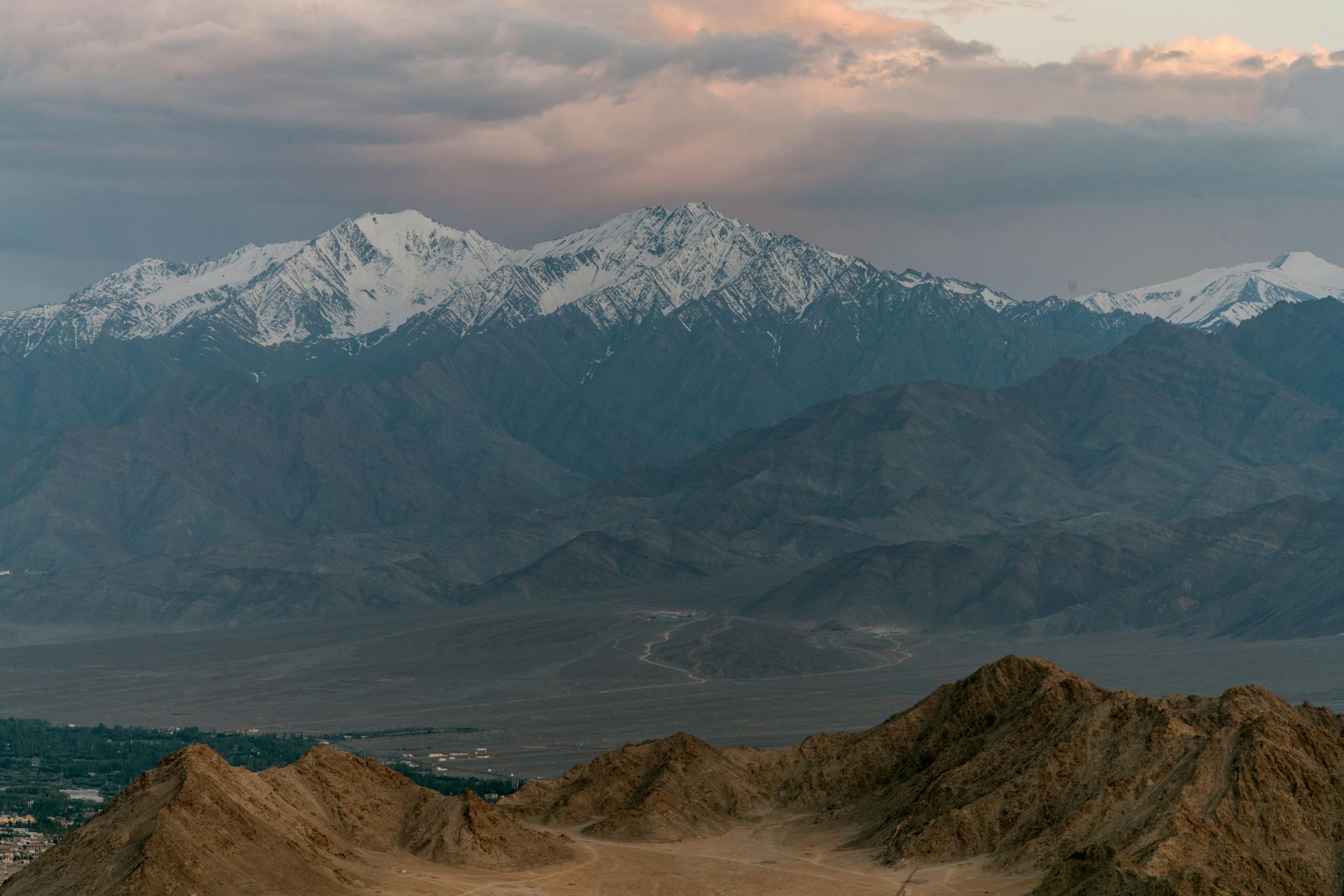 Picturesque view of high ridges with snowy peaks under cloudy sky at sundown