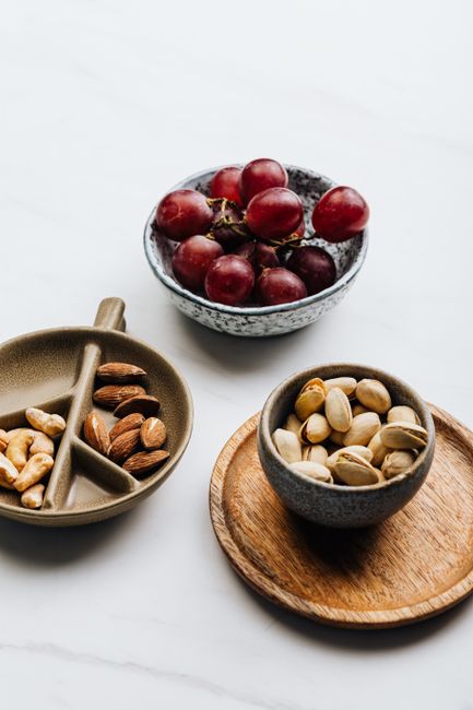 Aesthetic arrangement of bowls with grapes, almonds, cashews, and pistachios on white background. - healthy snacks for kids in Pakistan