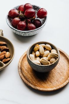 白色背景上，一个乡村风格的碗里盛着美味的开心果、杏仁和葡萄