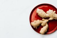 白色背景前，一块鲜姜根的特写镜头被置于一个鲜艳的红色盘子上