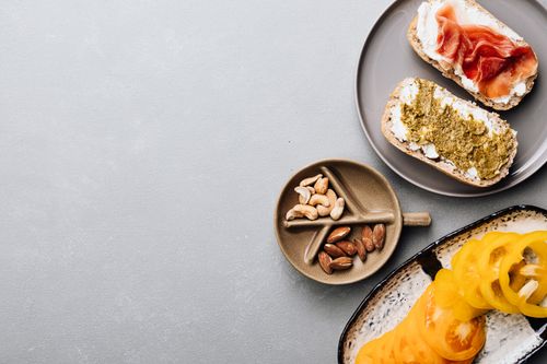Free Top view of a gourmet breakfast spread with toast, prosciutto, nuts, and sliced vegetables on a gray background. Stock Photo