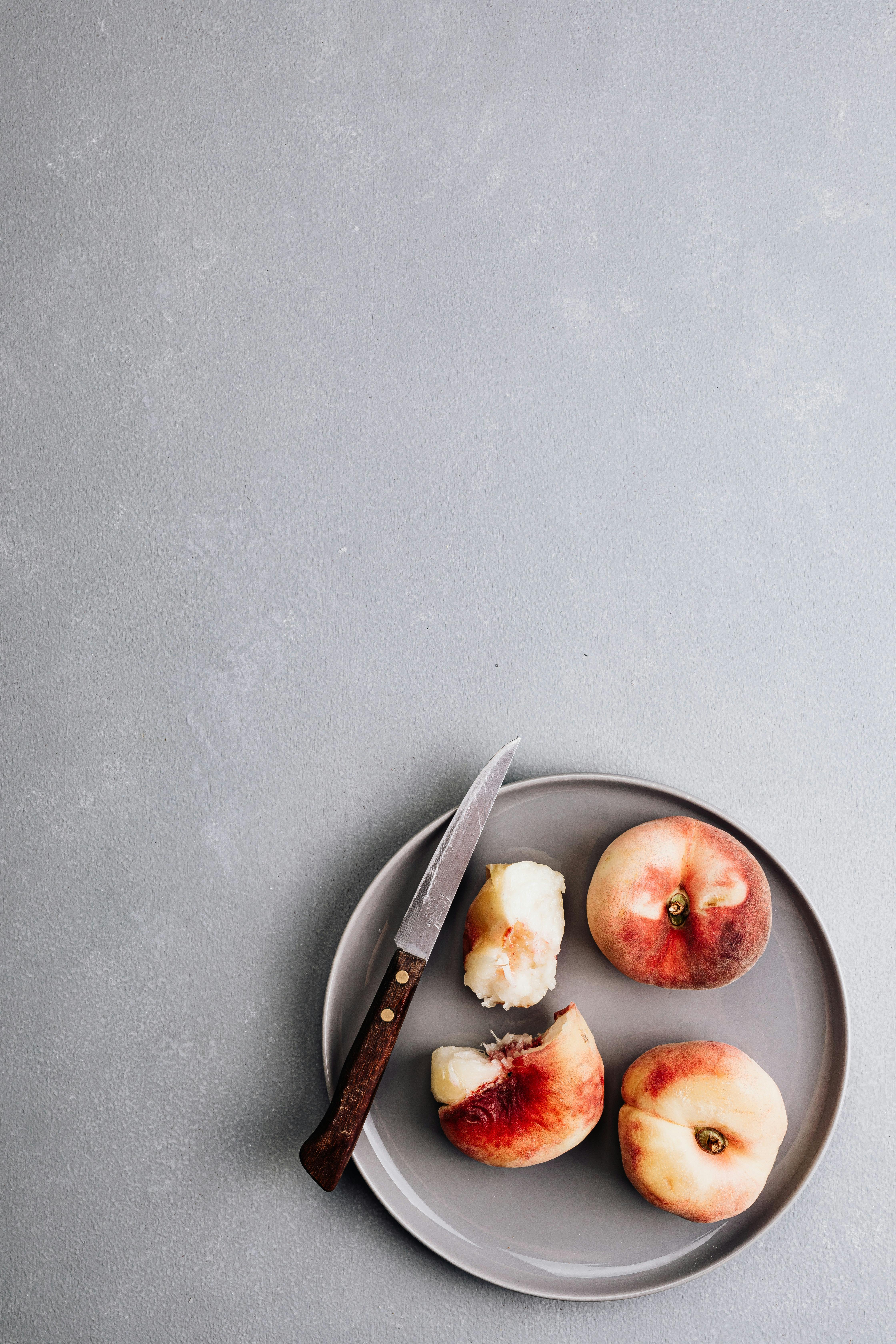 Top view of peaches on a gray plate with knife on textured background, perfect for food themes.