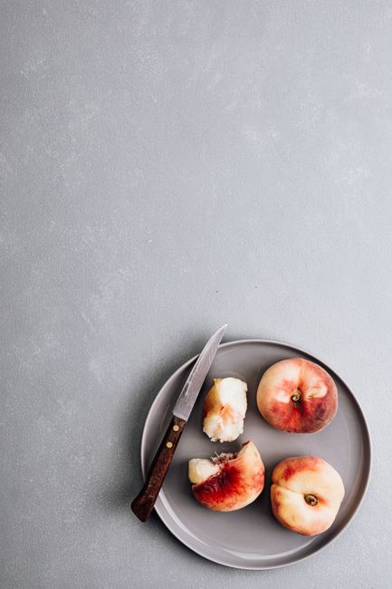 Top view of peaches on a gray plate with knife on textured background, perfect for food themes.