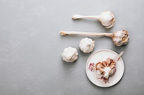 Free Top view of fresh garlic bulbs and cloves on a gray background with a saucer, ideal for food photography. Stock Photo