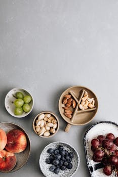 A flatlay of fresh fruits and nuts on a gray surface, offering healthy snacking options.