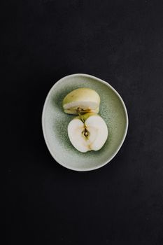 一块苹果片优雅地置于绿色盘子中，盘子衬着黑色背景，展现了极简主义的美食摄影