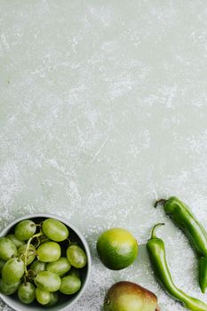 绿色水果和蔬菜，包括葡萄、酸橙、梨和辣椒，平铺在纹理背景上