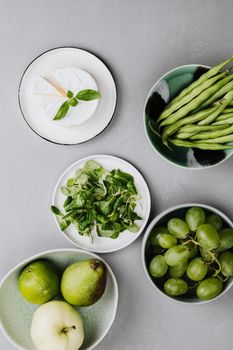 A creative flat lay of assorted green fruits, vegetables, and cheese on plates.