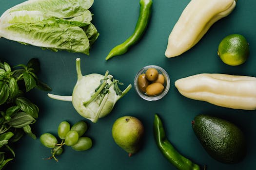A flat lay of fresh green vegetables and fruits on a green background, showcasing healthy eating.
