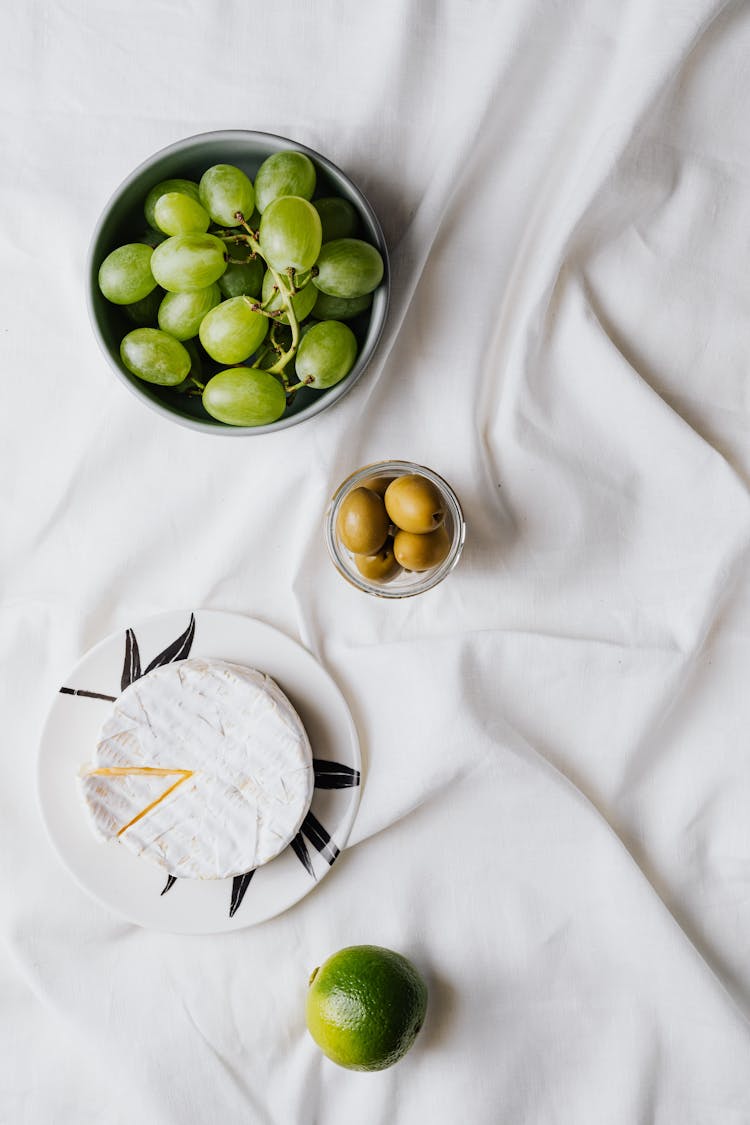 Fruits And Cheese On Tableware Over A White Cloth