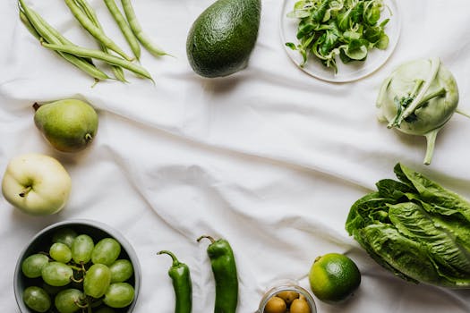 Top view of assorted fresh green vegetables and fruits arranged on a white background for healthy eating concept.