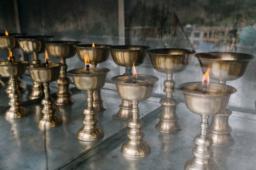 Free Rows of decorative shiny bowls with flaming candles on metal table in aged Asian temple Stock Photo