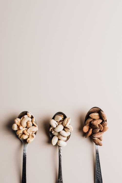 Free Three vintage spoons filled with assorted nuts on a beige background showcasing almonds, cashews, and pistachios. Stock Photo