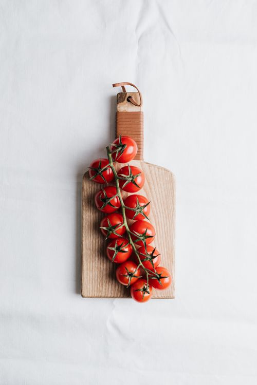 Free Fresh cluster of cherry tomatoes on a wooden cutting board with clean white background. Stock Photo