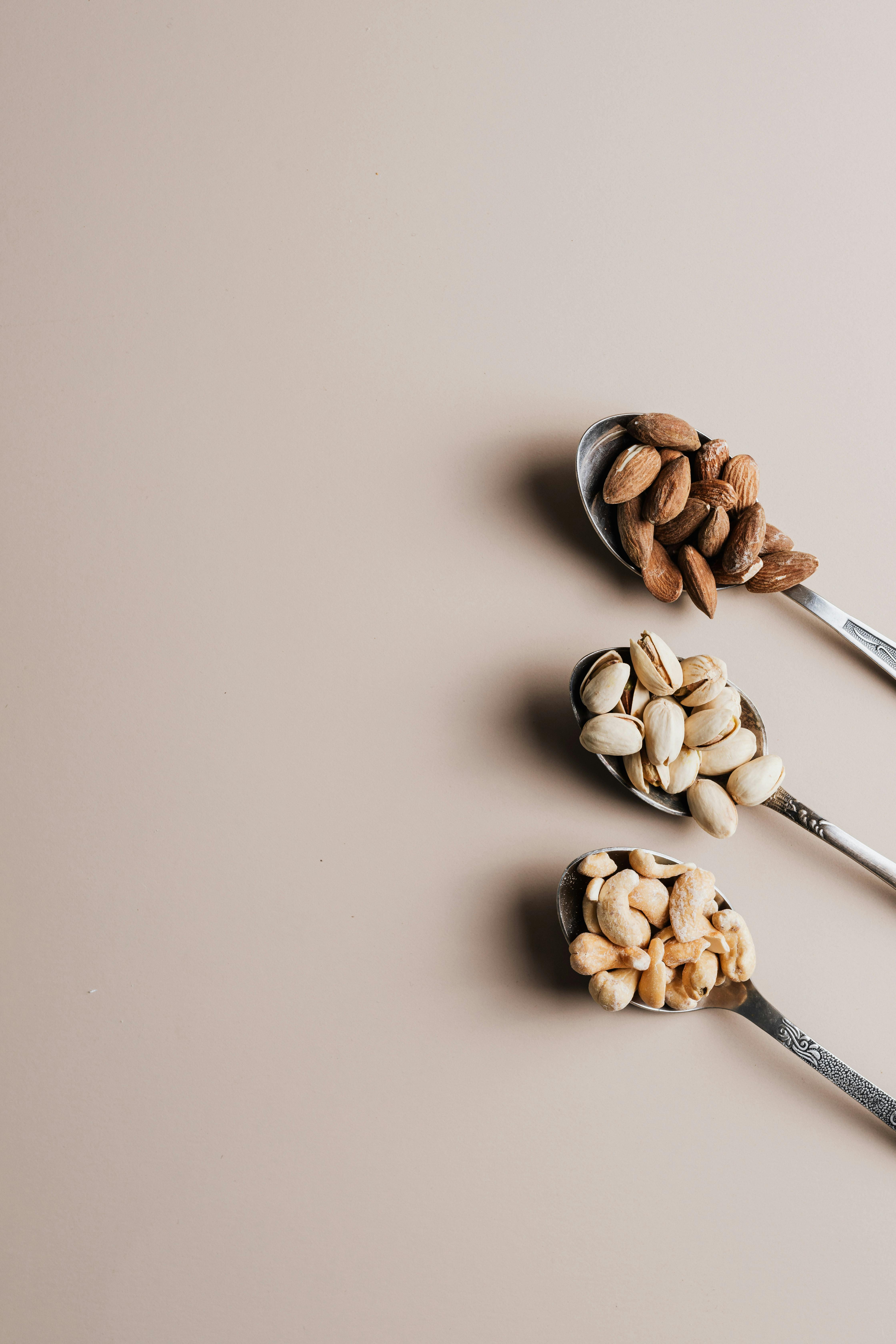 Flat lay of assorted nuts on spoons with empty copy space, perfect for healthy food concepts.