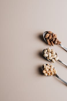Flat lay of assorted nuts on spoons with empty copy space, perfect for healthy food concepts.