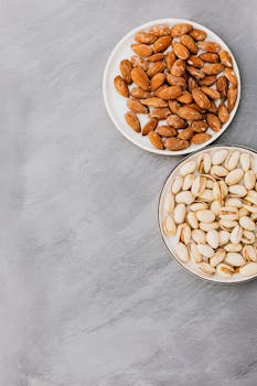 Flat lay of almonds and pistachios in bowls on a gray textured surface with copy space.