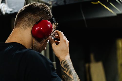 Free Close-up of a man adjusting safety glasses with red earmuffs in an indoor setting. Stock Photo
