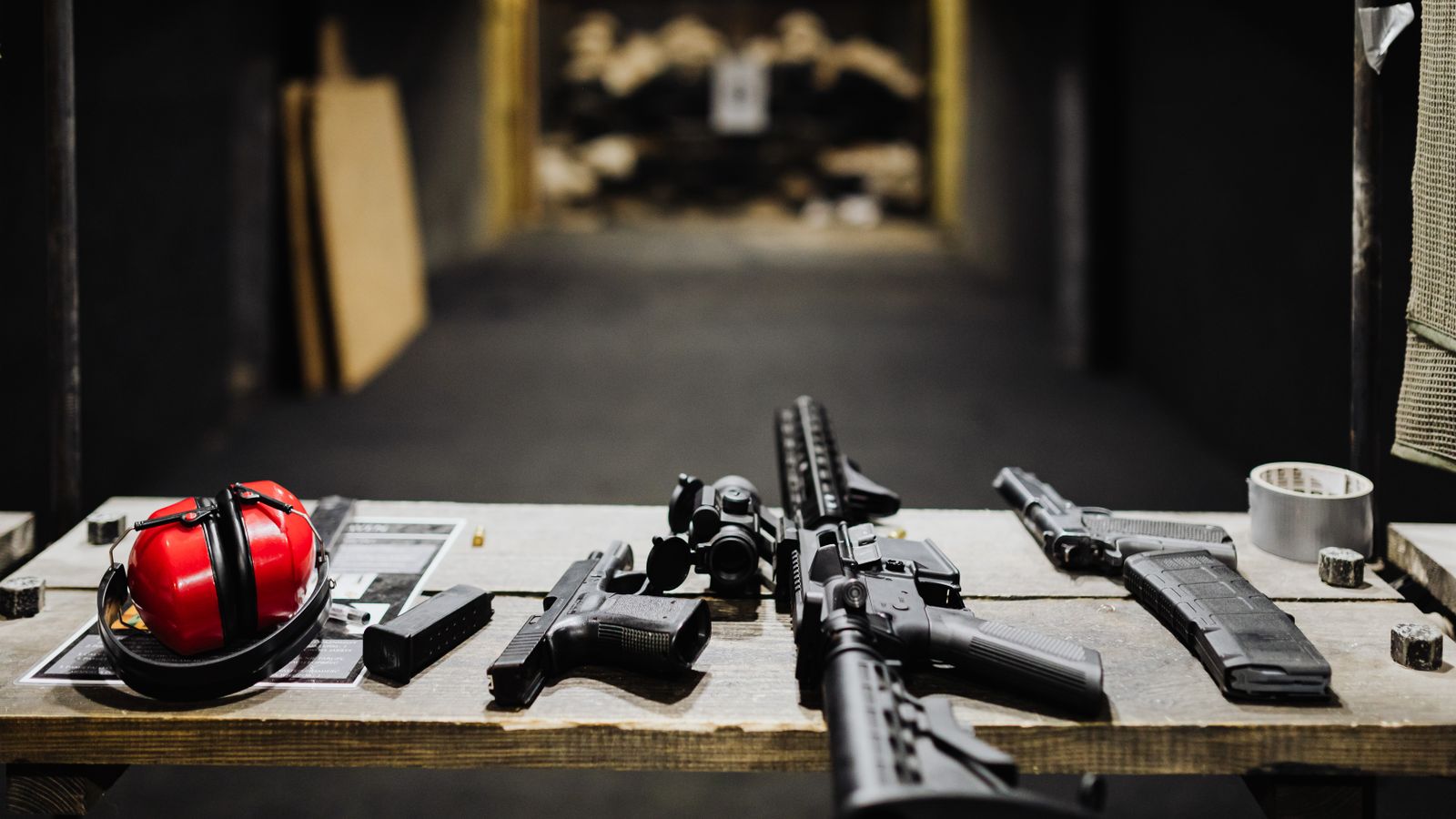 A selection of firearms and safety gear on a table at an indoor shooting range.