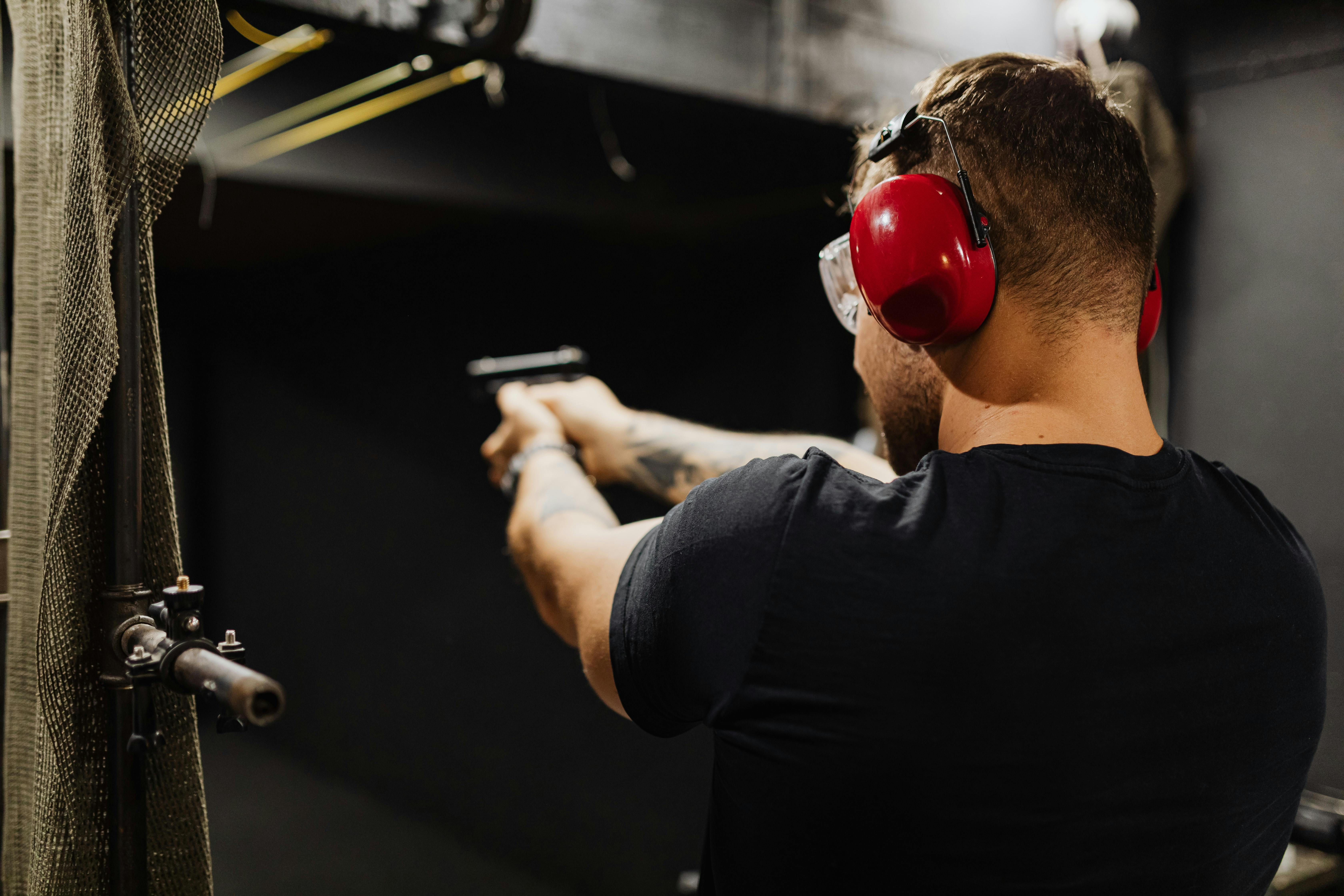 Adult male using handgun with earmuffs at indoor shooting range, focusing on target practice.