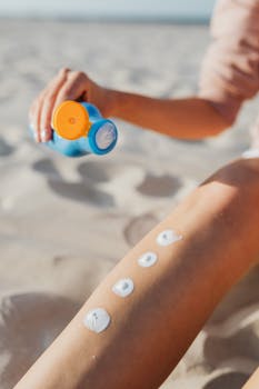 Woman applying sunscreen lotion on leg at the beach. Summer skincare routine for sun protection outdoors.