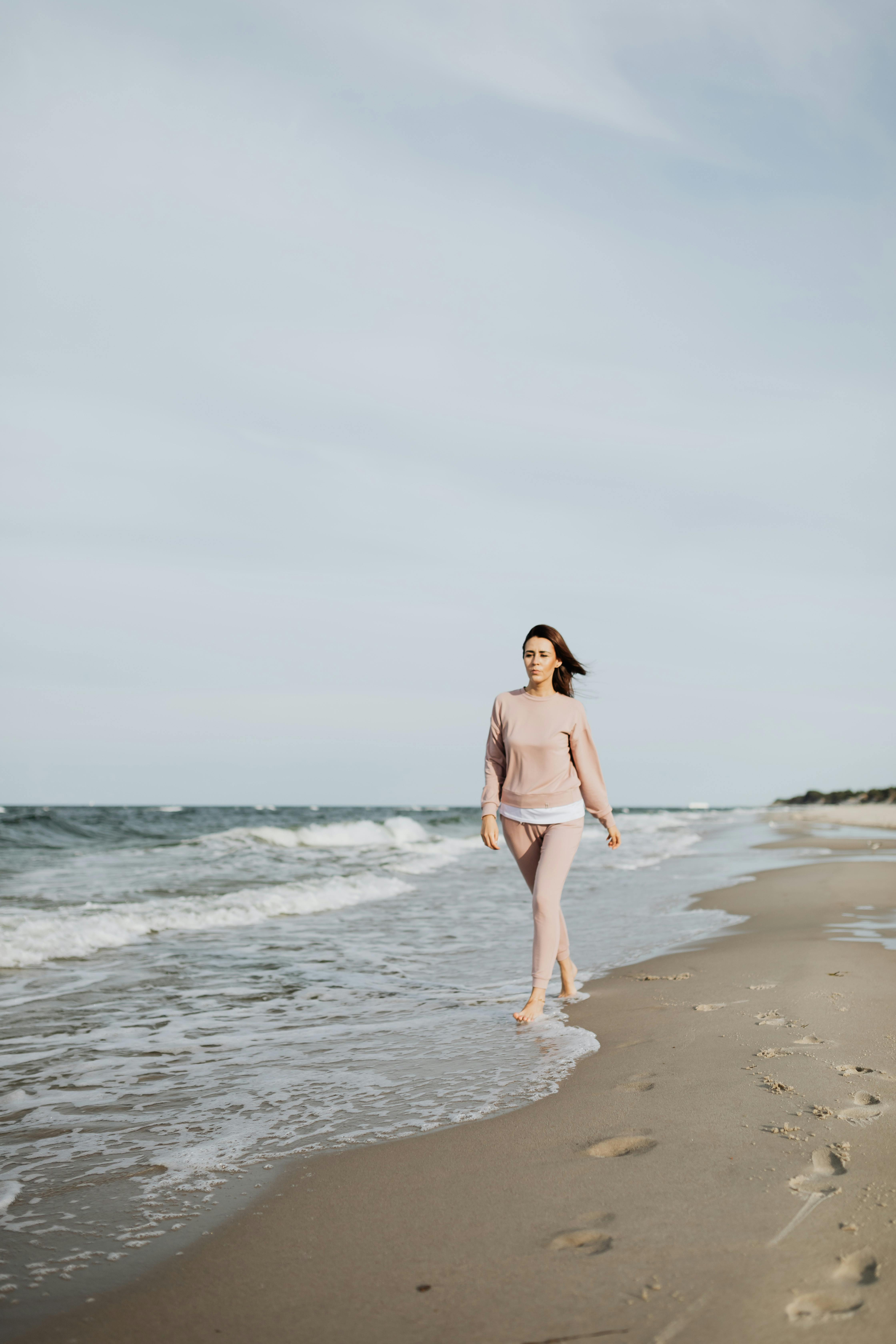 一名身穿粉红色服装的女子沿着宁静的海岸平静地散步