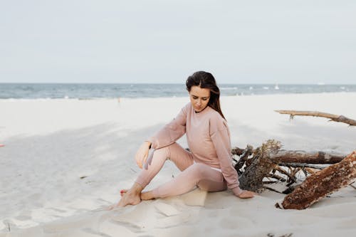Free Woman in Pink Long Sleeve Shirt Sitting on White Sand Stock Photo