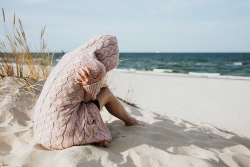Free Solitary woman in pink knitted sweater on a tranquil beach setting. Stock Photo