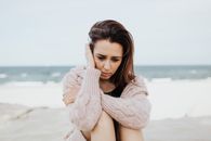 一个女人穿着粉红色毛衣，独自坐在海滩上沉思