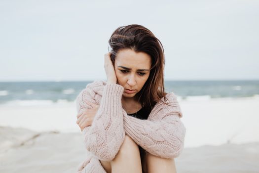 一个女人穿着粉红色毛衣，独自坐在海滩上沉思