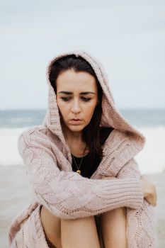 一位穿着粉色针织衫的女人若有所思地坐在海边，沉浸在反思的情绪中