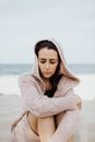 一位穿着针织衫的女人在海边静坐，陷入深思，与孤独为伴