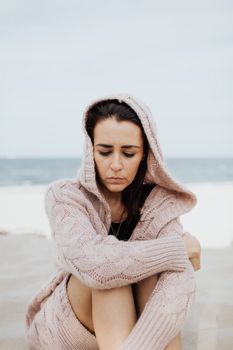 一位穿着针织衫的女人在海边静坐，陷入深思，与孤独为伴