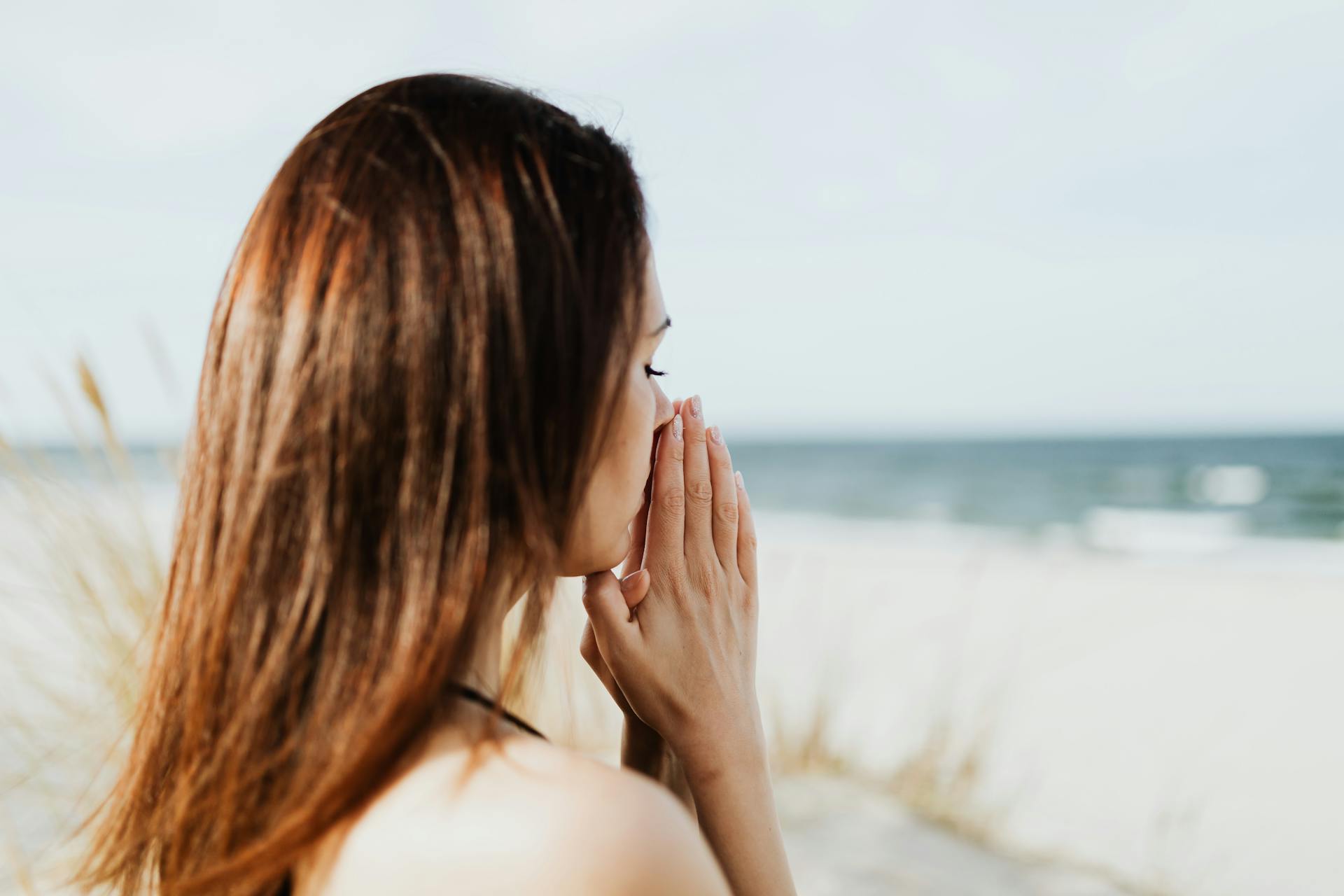 Woman meditating by the beach with hands together, embracing tranquility and peace.