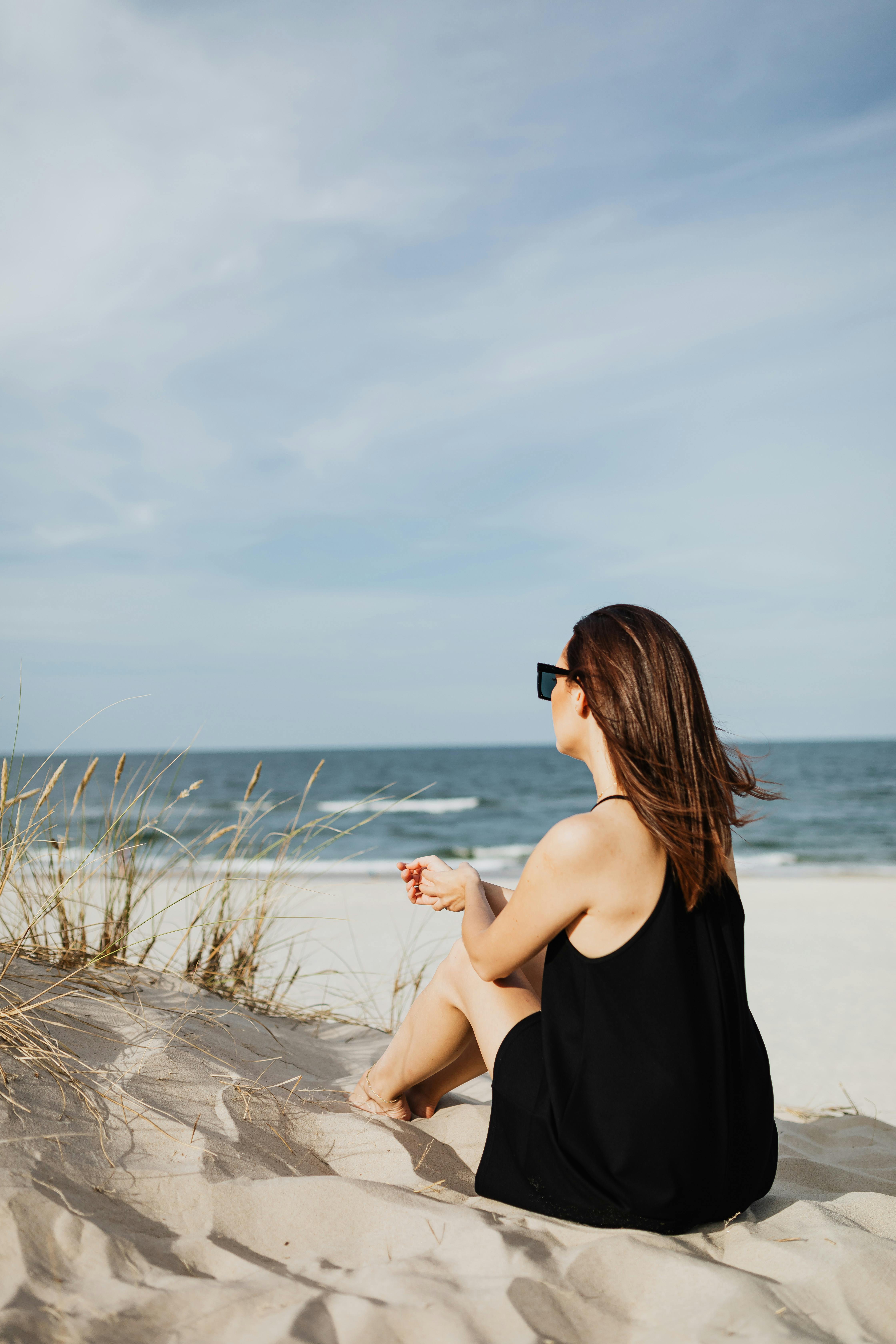一个女人坐在沙滩上，背对着镜头，凝视着晴朗天空下的海洋
