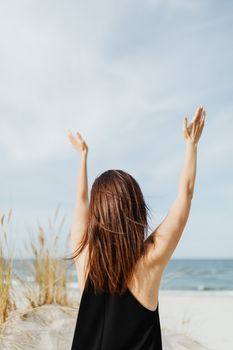 一名女子在蓝天下的沙滩上快乐地举起双臂