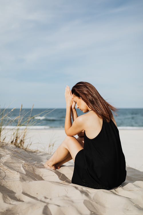 Free Woman Sitting on White Sand with her Hands Pressed Together Stock Photo