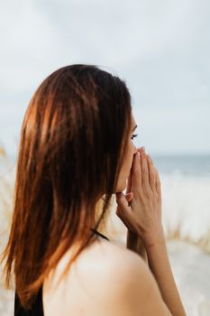 一名妇女在海滩上双手合十祈祷，这是她表达信仰的侧面图