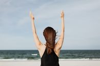 一名女子面对大海，高举双臂站在海滩上，象征着自由和欢乐