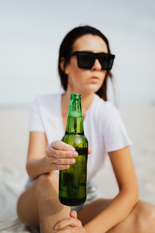 Woman in White T-shirt Holding Green Glass Bottle