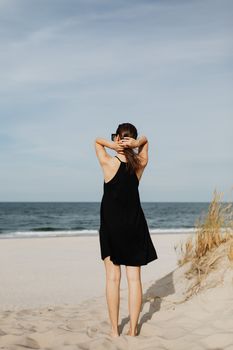 一名身穿黑色连衣裙的女子站在沙滩上，凝视着大海