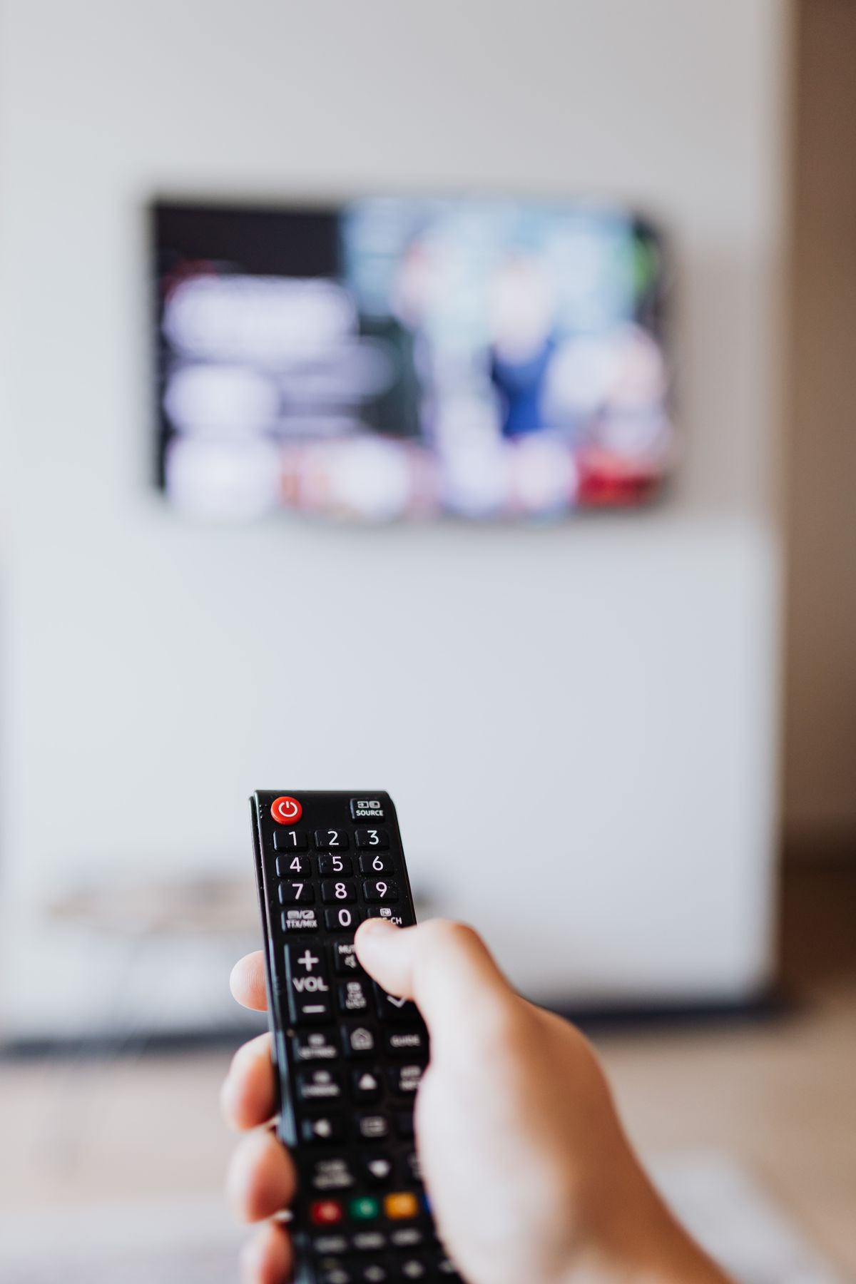 Person holding a black remote control while watching television at home, illustrating device use in Vancouver