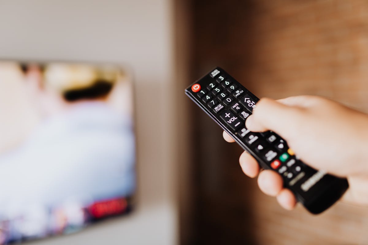 Mano che indica un telecomando rivolto verso uno schermo TV