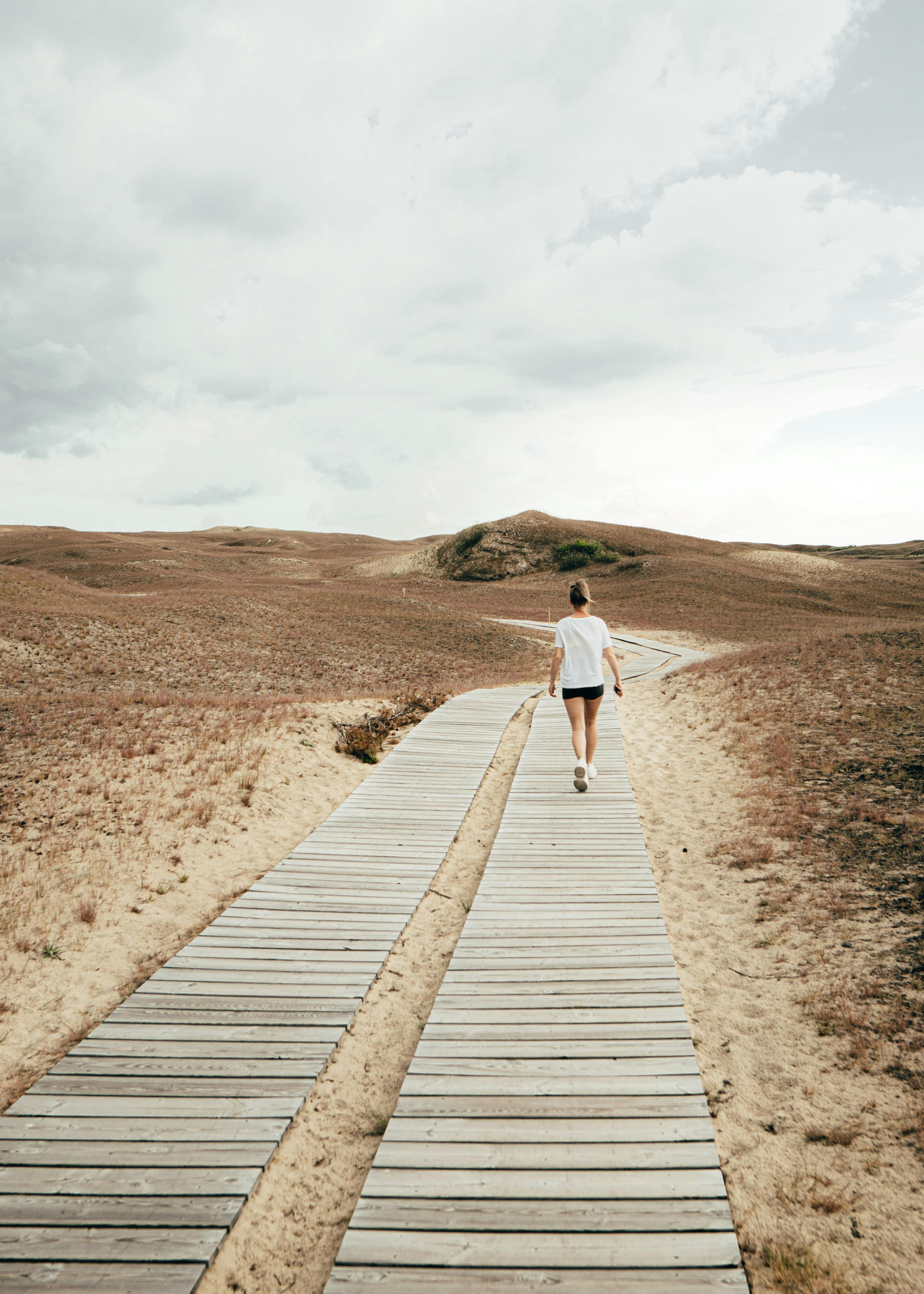 一个女人孤独地走在木制小路上，穿过阴天里沙漠般的风景