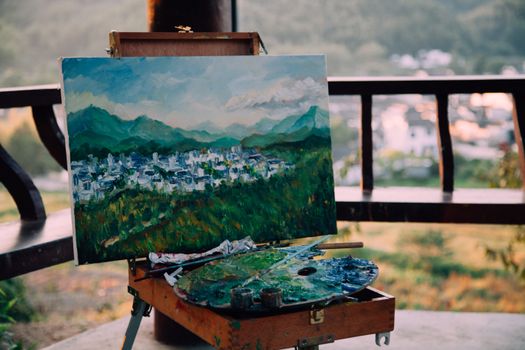 Creative artwork representing mounts and houses under sky near paint palette in wooden arbor