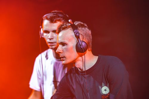 Free Two DJs perform live with headphones on, creating an immersive music experience under dramatic lighting. Stock Photo