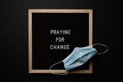 Praying for change text in frame near mask placed on blackboard